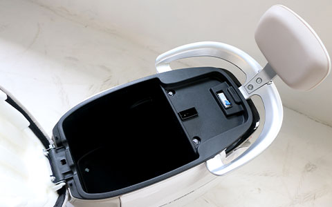 Electric Scooter | Under-Seat Storage Compartment Detail Open under-seat storage compartment of white electric motorcycle, showing hidden storage space