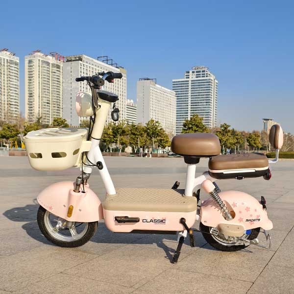 A pink and beige electric bicycle, placed in an open square with tall buildings, green trees and blue sky in the background.